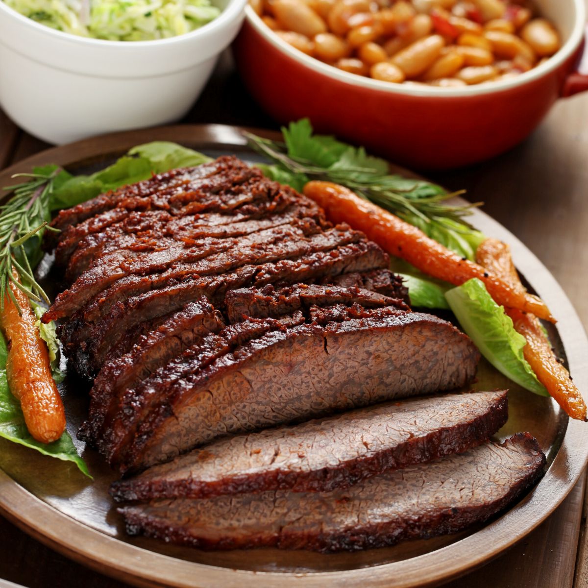 Beef Brisket mit Karotten, Bohnen und Krautbeilage im Hintergrund.